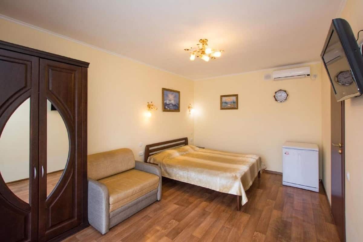 Una habitación pequeña y acogedora con cama, sofá, una mesita y televisión.