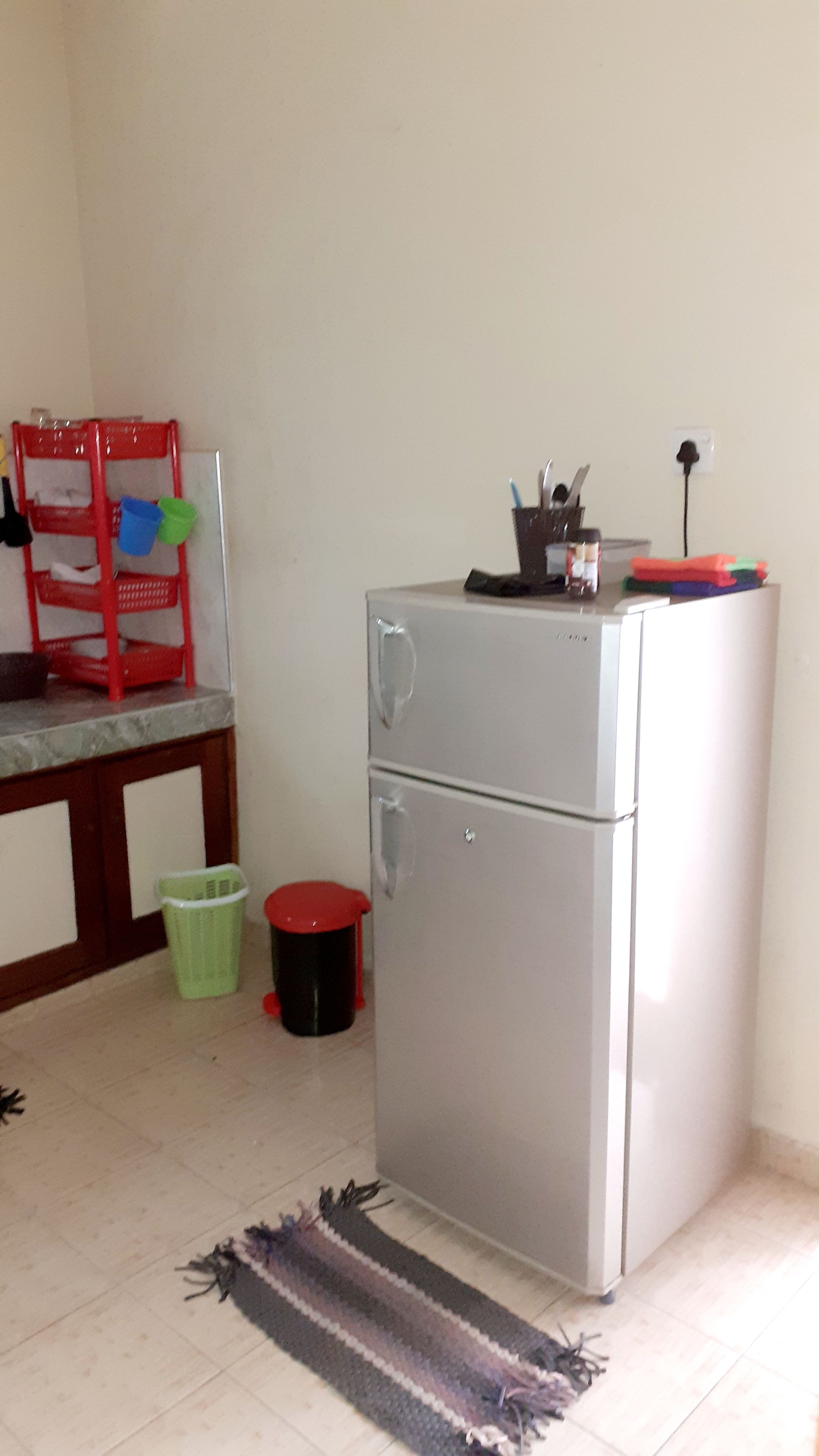 Una kitchenette compacta con refrigerador, un lavamanos pequeño y una silla roja.