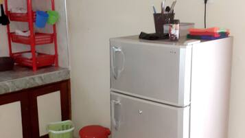 Una kitchenette compacta con refrigerador, un lavamanos pequeño y una silla roja.