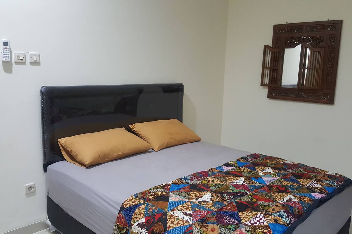 Een bed met een donker hoofdbord, twee kussens en een kleurrijke quilt.