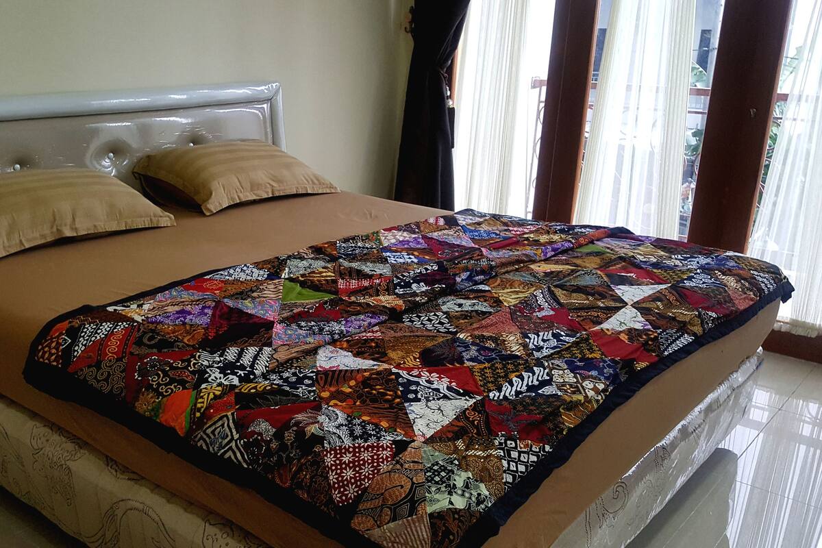 Een bed met een sprei en twee kussens, een houten hoofdbord en een raam met gordijnen.