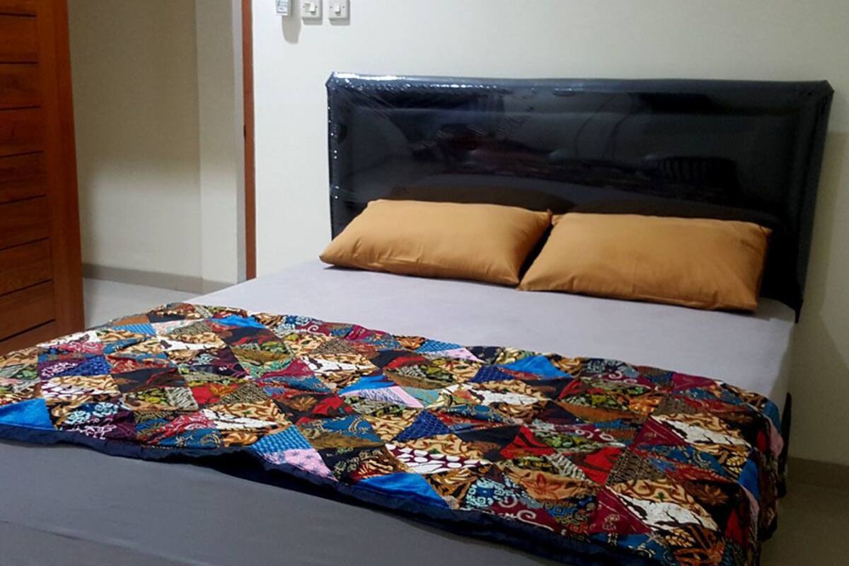 Een bed met een kleurrijke sprei, een zwart hoofdbord en twee bruine kussens.
