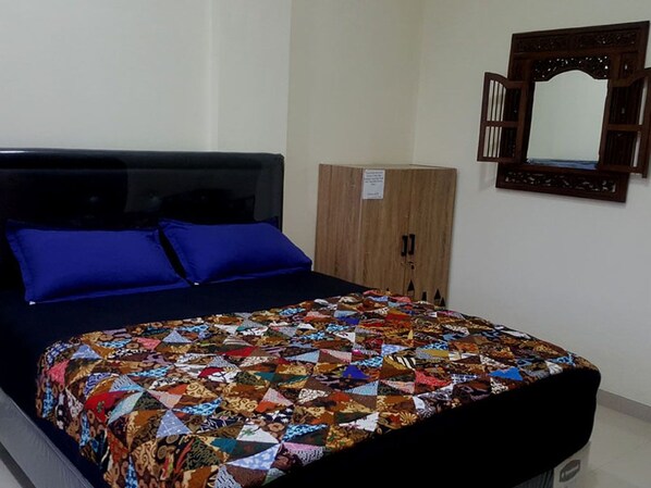 A bed with a colorful quilt, a wooden wardrobe, and a mirror on the wall. - Family Home Ratmono JIH (Depok)