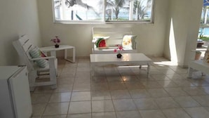 A bright room with a white sofa, a small table, and a window with a view of palm trees and a pool. - La Casa de la Playa (Cuyutlan)
