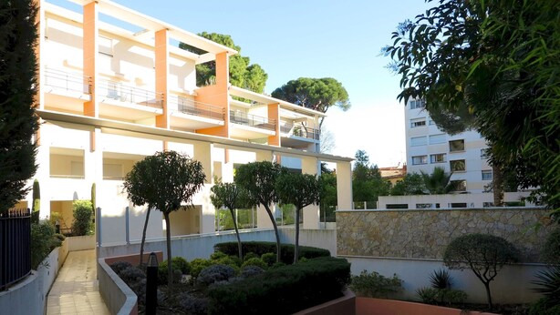 Un immeuble résidentiel à plusieurs étages, doté de balcons, d’un jardin aménagé et d’un mur en pierre.