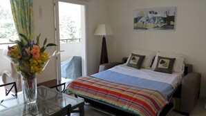 Une chambre d’hôtel avec un lit, une table ornée d’un vase de fleurs, une chaise, une lampe et un tableau accroché au mur.