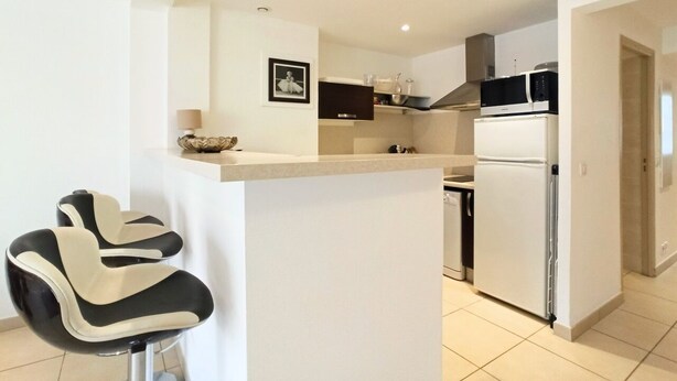 A modern kitchen with a refrigerator, microwave, and a small island with bar stools. - Viva Riviera 2 Bedrooms 2 Bathrooms Rue Florian (Cannes)
