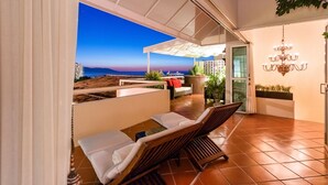Un espace extérieur moderne, aménagé pour se détendre, avec vue sur la mer au coucher du soleil.