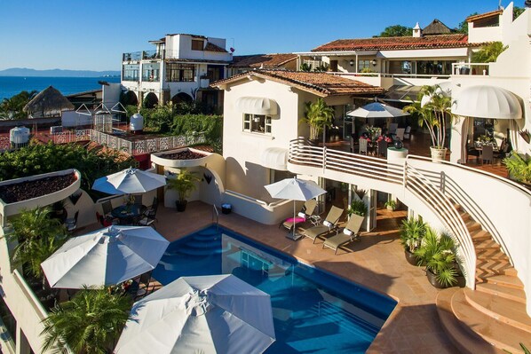 A pool area with lounge chairs and umbrellas, a staircase, and a view of the sea.