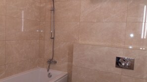 Bathroom features a standalone bathtub with a showerhead and chrome faucet, set against a wall with large, smooth tiles.