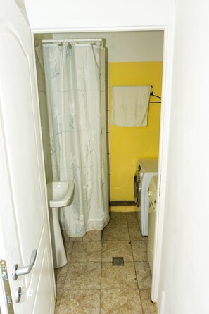 Een compacte badkamer met een douche, wastafel en een wasmachine.