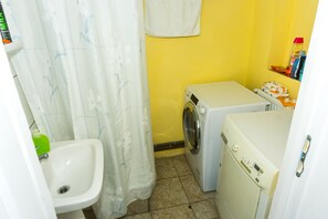 Een kleine badkamer met een wastafel, een wasmachine en een douchegordijn.