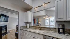 A modern kitchen with white cabinetry, a granite countertop, a built-in dishwasher, and a fireplace.