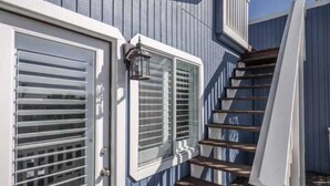 A staircase leading to a deck with a railing, a door with a window, and a wall with vertical siding.