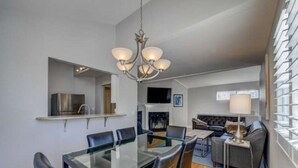 A modern dining area with a glass table and chairs, a chandelier, and a kitchen area with a built-in oven and microwave.