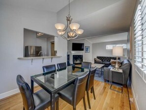 A modern dining area with a glass table and chairs, a chandelier, and a kitchen area with a built-in oven and microwave.