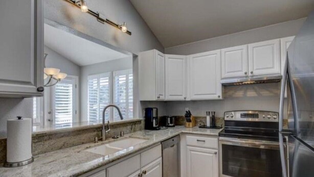 A modern kitchen with white cabinets, a stainless steel refrigerator, a built-in oven, and a granite countertop.