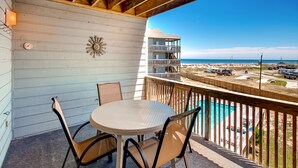 A balcony with a table and chairs, overlooking a beach and a parking area. - Semi-Oceanfront Condo w/ Private Balcony, Resort Pool, Elevator, Beach Access (Rodanthe)
