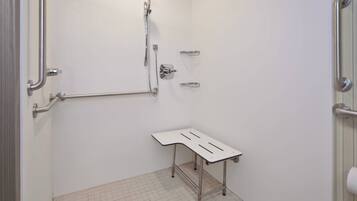 A bathroom with a shower, grab bars, a white sink, and a toilet.