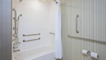 A bathroom with a bathtub, grab bars, a showerhead, and a towel rack.