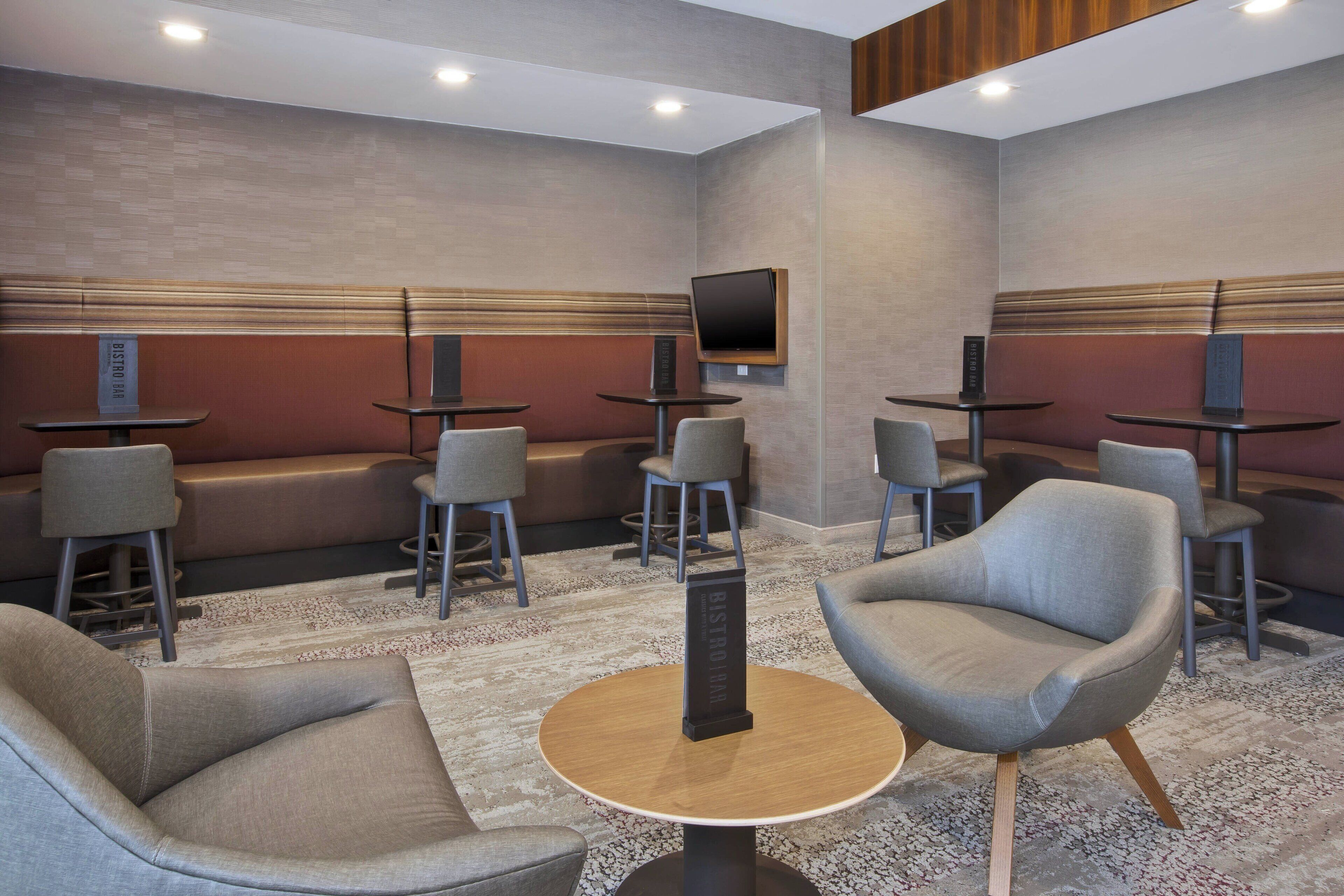 Ein moderner Lounge-Bereich mit Sofas, Sesseln und Tischen, mit einem an der Wand befestigten Flachbildfernseher.
