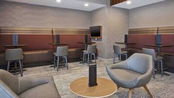 Ein moderner Lounge-Bereich mit Sofas, Sesseln und Tischen, mit einem an der Wand befestigten Flachbildfernseher.