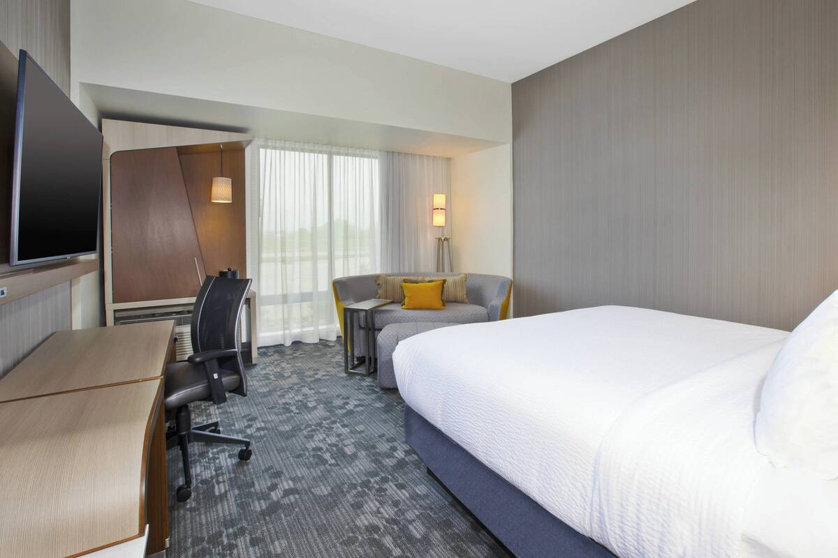 Een hotelkamer met een groot bed, een bureau met stoel, een bijzettafeltje met stoel en een aan de muur bevestigde televisie.
