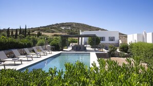A poolside area with lounge chairs, a pergola, and a view of a hill. - Villa Anemos (Ampelas)