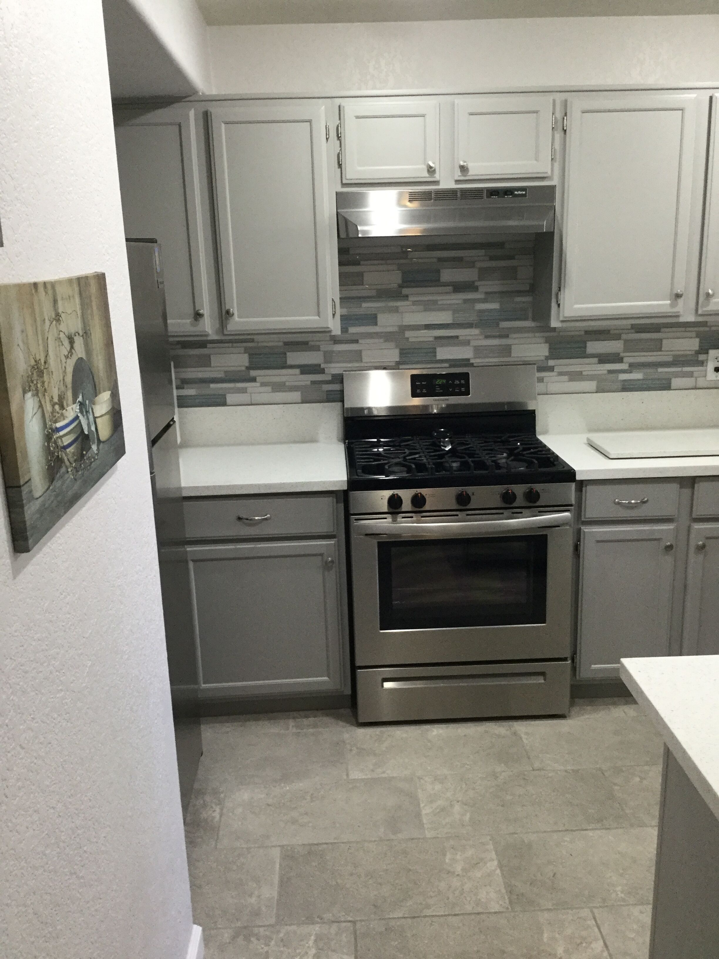 A kitchen with stainless steel appliances, grey cabinets, and a tiled backsplash.