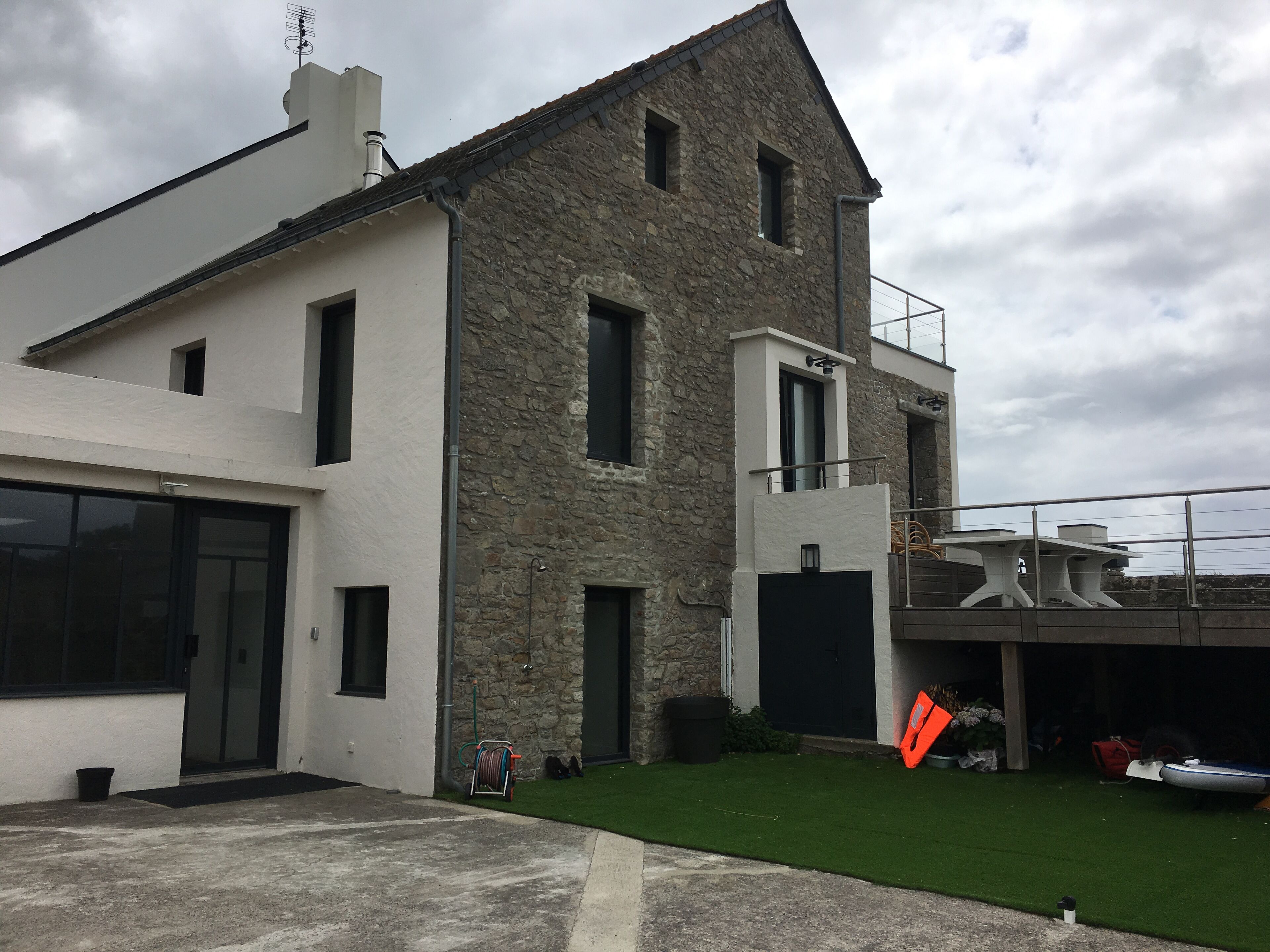 Ein modernes, zweistöckiges Haus mit Natursteinfassade, großen Fenstern und einer Garage.