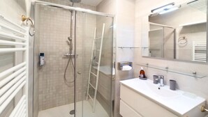 Ein modernes Badezimmer mit einer gläsernen Duschkabine, einem weißen Waschbecken mit Spiegel darüber und einem Handtuchhalter links.