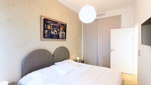 Ein ordentlich bezogenes Bett mit Kopfteil, einer Nachttischlampe und einem Wandbild.