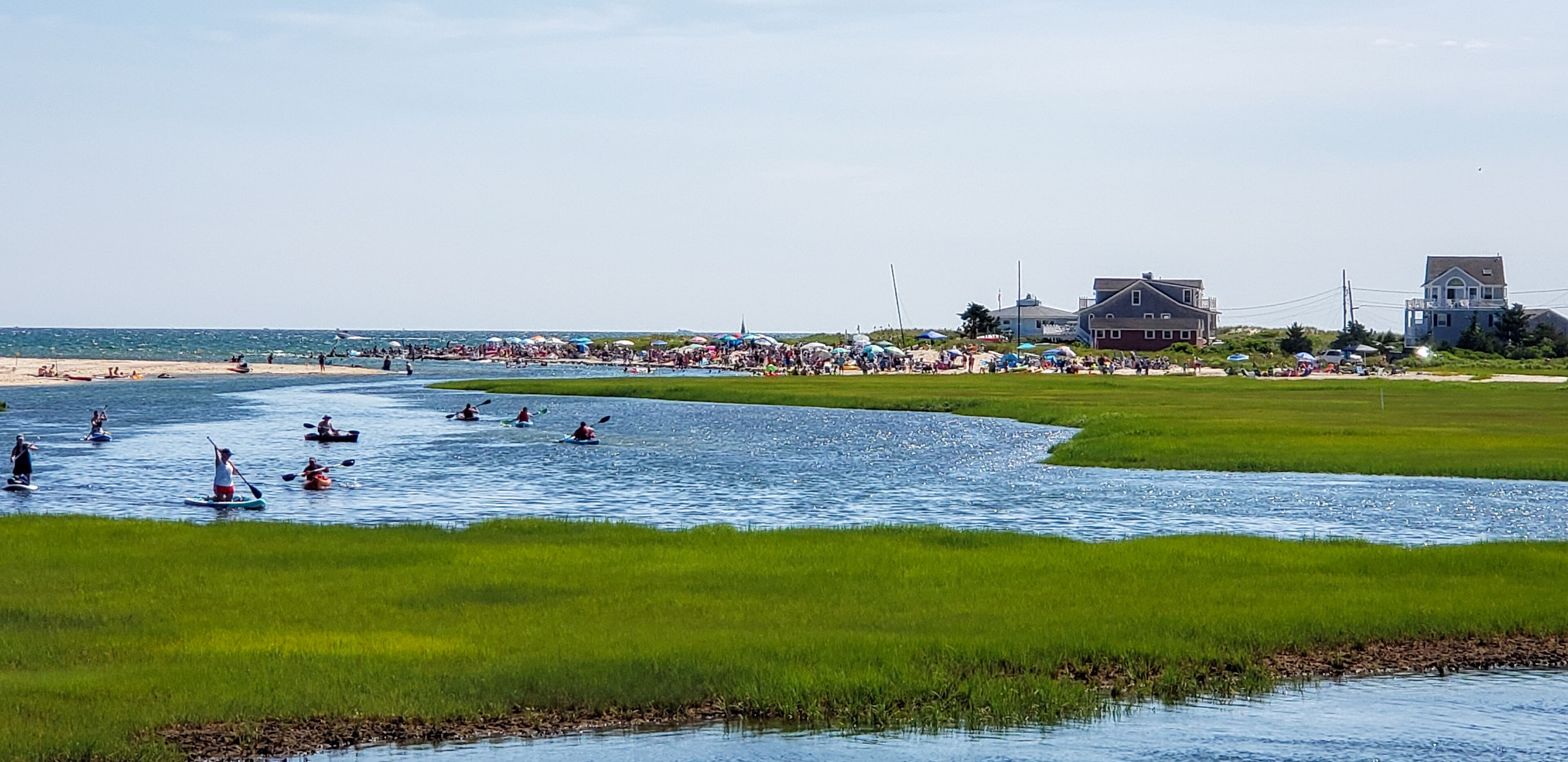 A riverside area with kayaks, a beach, and houses in the background.
