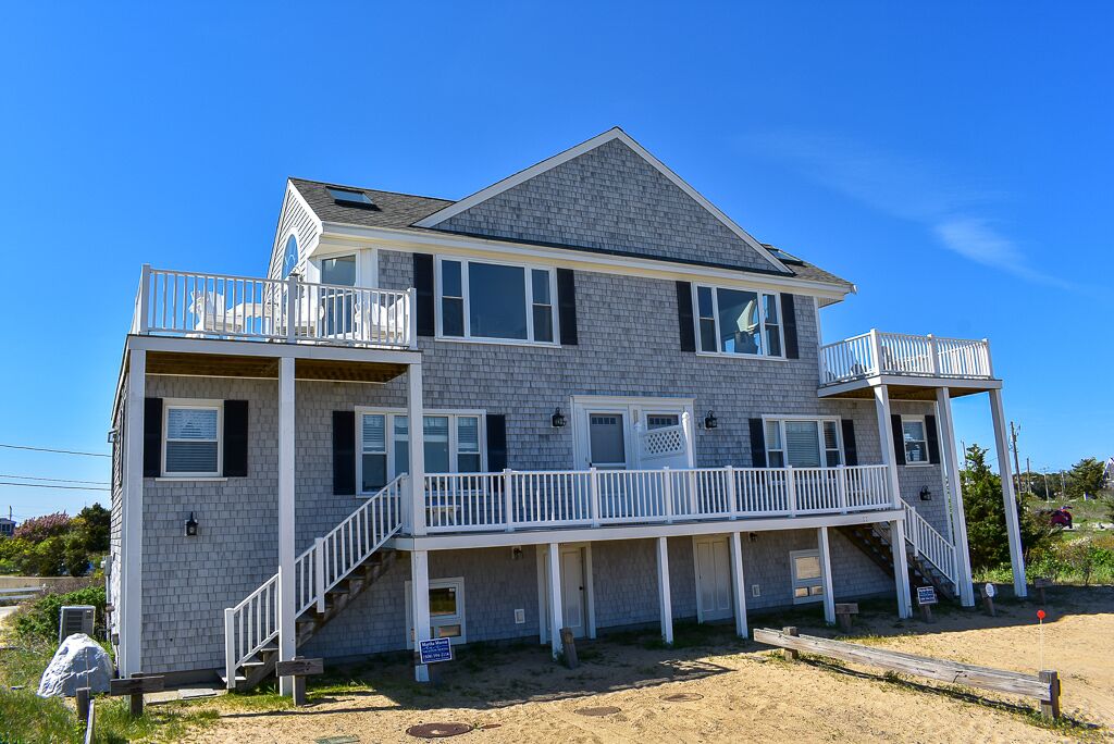 Une maison à deux étages située en bord de mer, dotée d’un balcon et d’une véranda couverte.