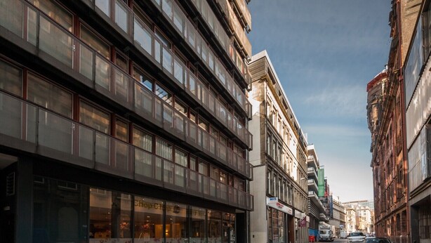 En gatubild med moderna byggnader, en butik med stora glasf önster som syns tydligt och en klar himmel.
