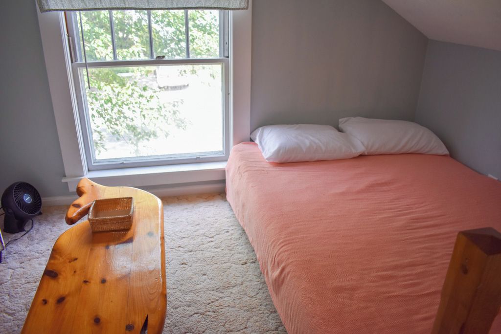 Une chambre avec un lit, une fenêtre, un bureau en bois et un ventilateur.