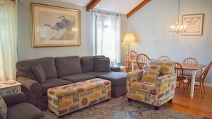 A living room with a sofa, ottoman, and patterned armchairs, a dining table with chairs, a chandelier, and a framed picture on the wall. - Dennis Port beach home less than two tenths of a mile to Haigis public beach (Dennis Port)