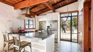 A kitchen with a large island, white cabinets, a stainless steel refrigerator, and a view to the outside.