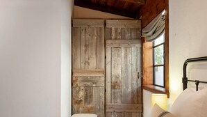 A bedroom with a wooden wardrobe, a window with curtains, and a bed with pillows.
