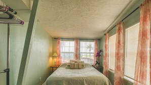 Un dormitorio con una cama, una mesita de noche, una lámpara y una ventana con cortinas.