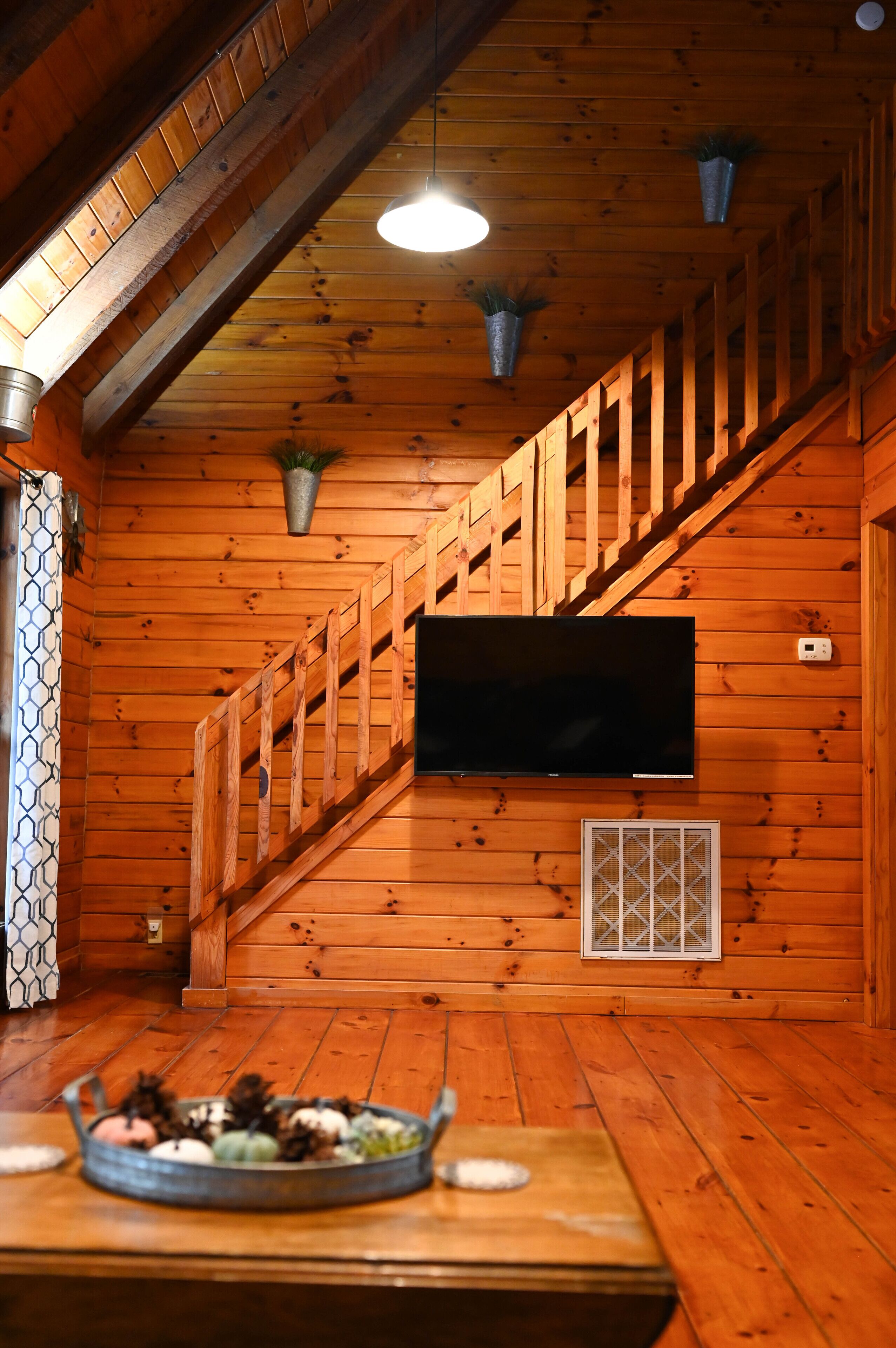 Ein Holzinnenraum mit an der Wand montiertem Fernseher, einer Treppe und einem Tisch mit Dekoration.