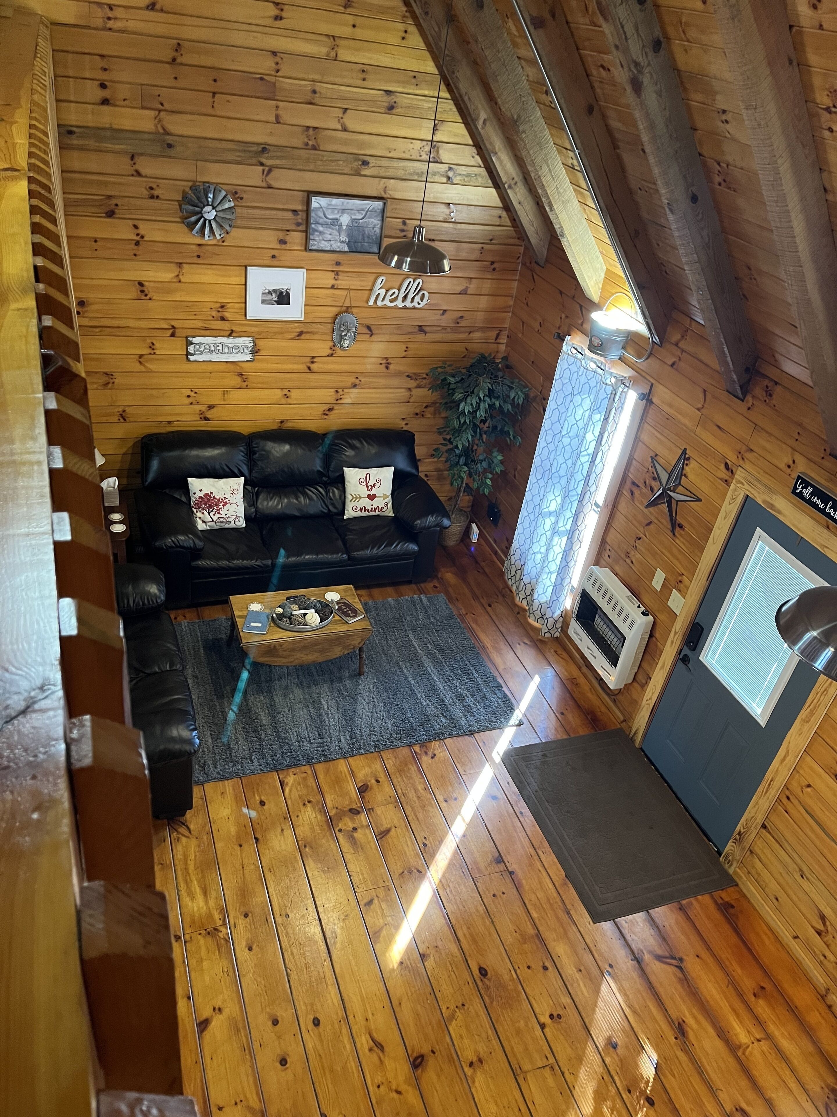 Interior acogedor de una cabaña con techo de madera, un sofá de cuero negro, una mesa de centro de madera y una puerta con ventana.