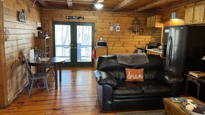 Un acogedor interior de cabaña con comedor, un sofá de cuero y una almohada con la palabra 'dream', una cocina con refrigerador y paredes de madera.