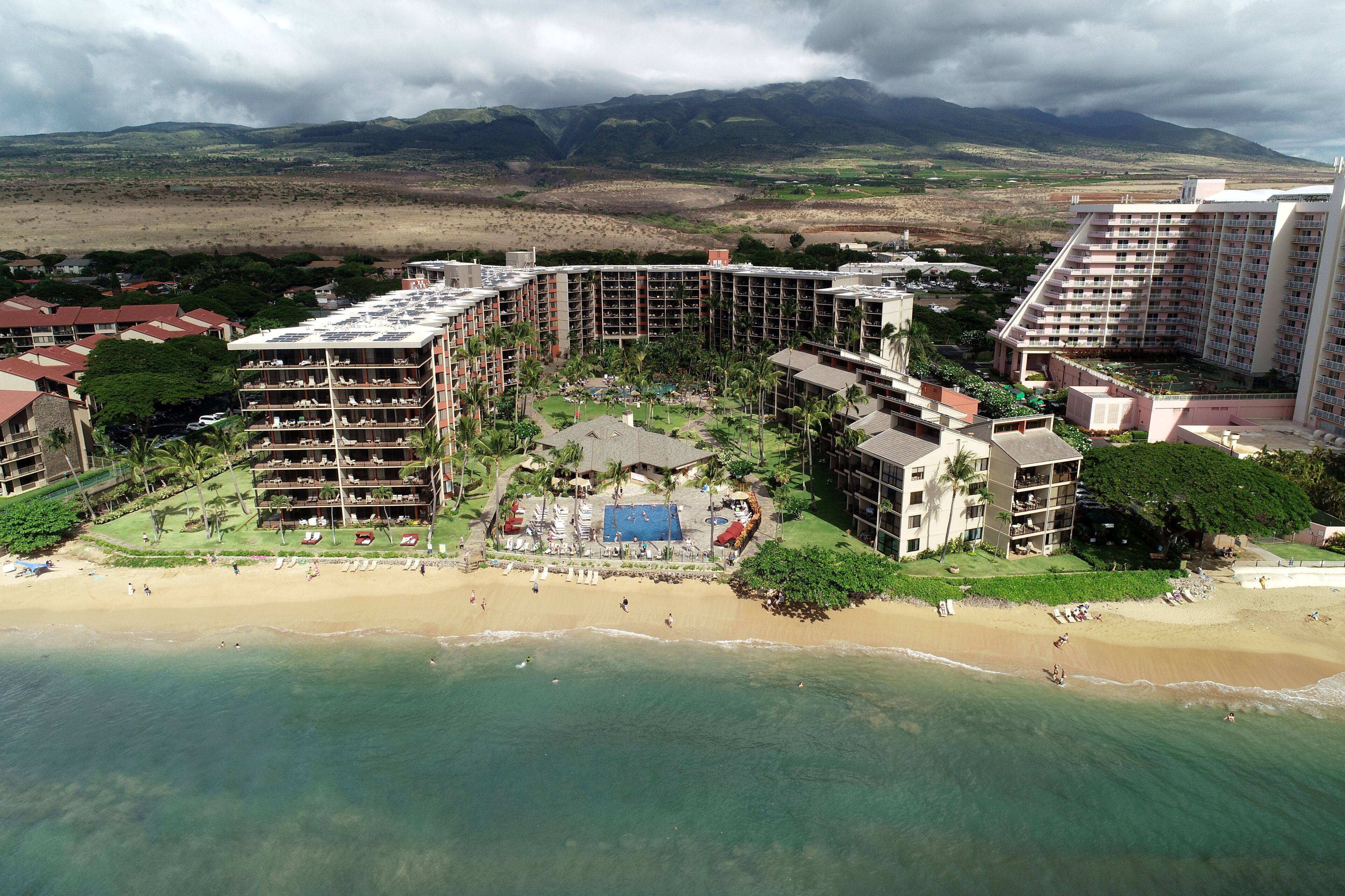 A resort with multiple buildings, a beach, and a mountainous backdrop.