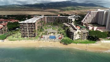 A resort with multiple buildings, a beach, and a mountainous backdrop.