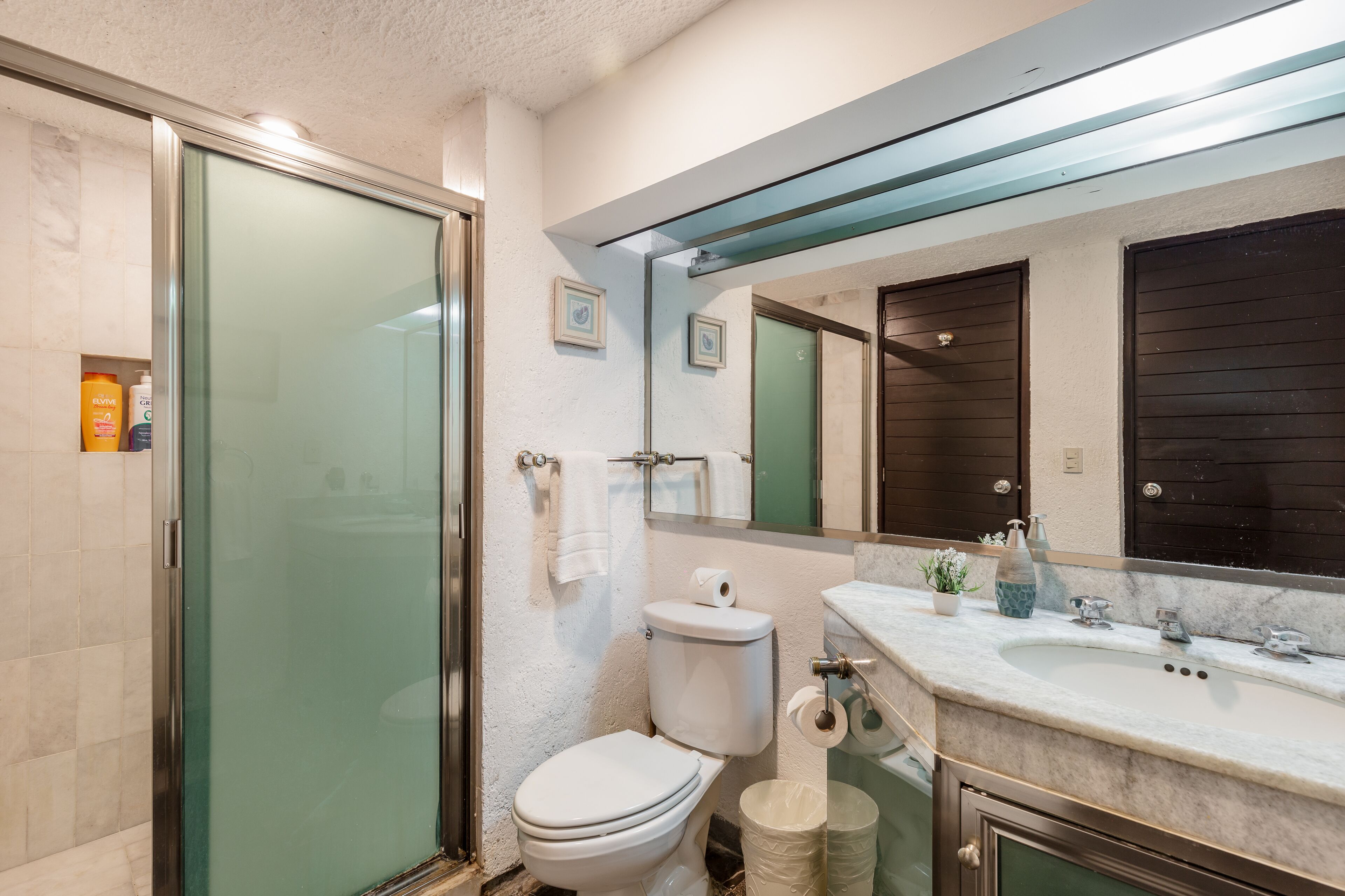 Ein Badezimmer mit Glasdusche, Toilette, Waschbecken mit Marmorplatte und großem Spiegel.