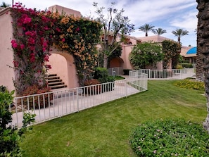 Stroll through lush gardens, surrounded by vibrant flowers and palm trees, along a paved pathway leading to a charming outdoor space.