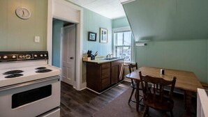 A kitchen with a white stove, wooden cabinets, a dining table with chairs, and a window with a view. - Ocean Breezes at Salty Air Suites, Suite C – New Balcony, 3BR, walk to the Beach (Old Orchard Beach)