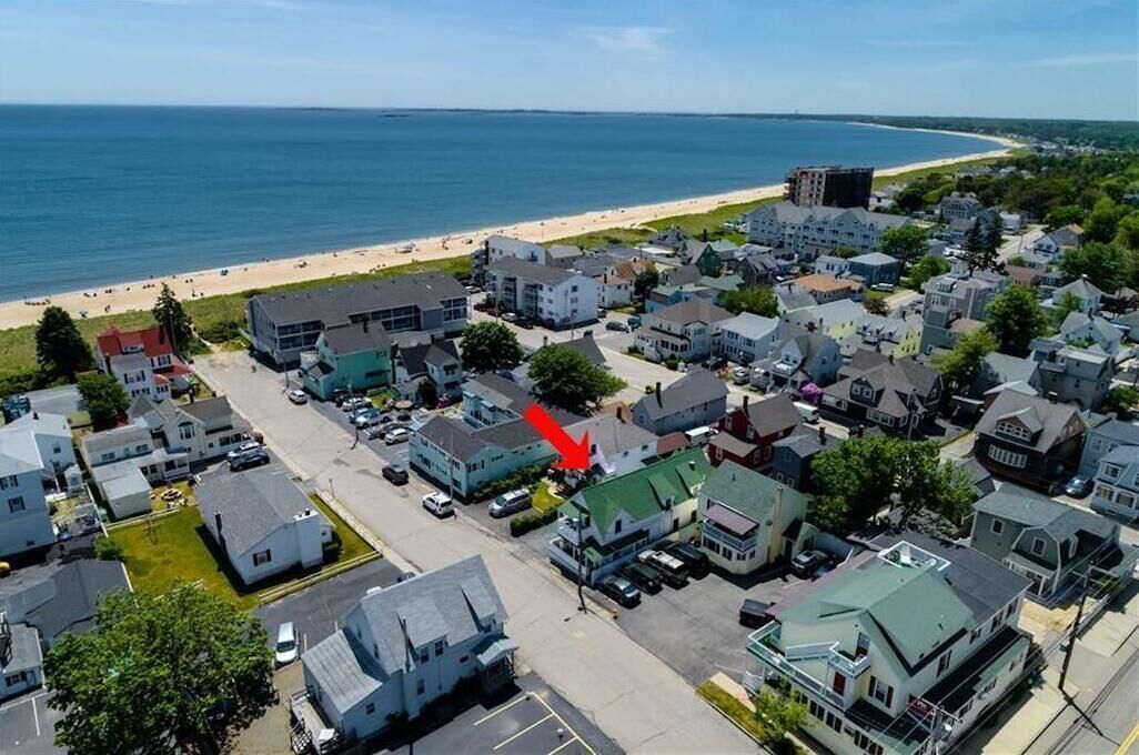 A coastal town with a beach, houses, and a prominent building with a red arrow pointing to it.