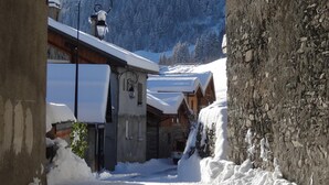 A narrow snow-covered alleyway with rustic buildings, a stone wall on the right, and a wooden building with a snow-covered roof on the left. - Spacious and comfortable chalet for 13 people - connected to Arcs 2000 in 20 minutes (Villaroger)